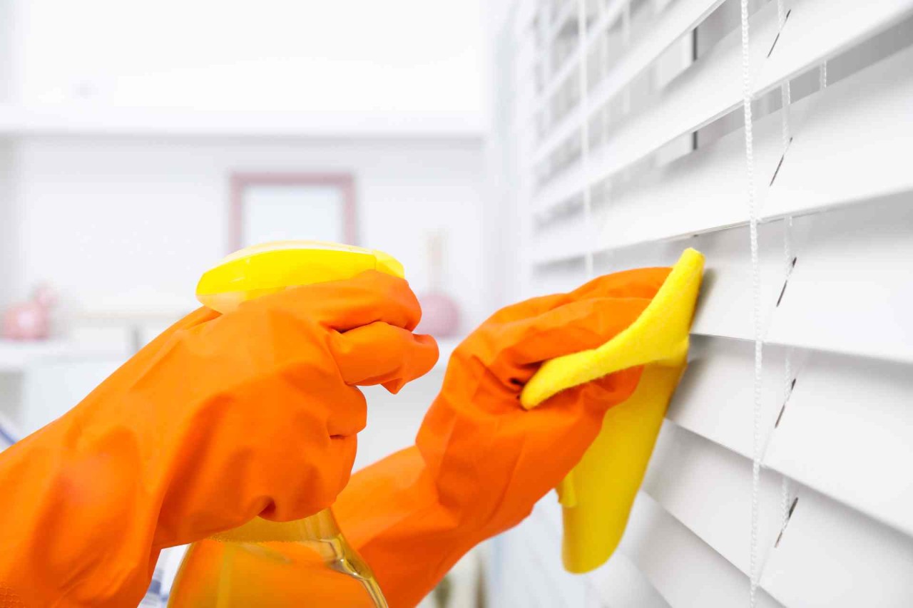 Person wearing bright orange gloves holding a yellow spray bottle and rag to clean their blinds at Window Decor of Fairfax near Fairfax, VA